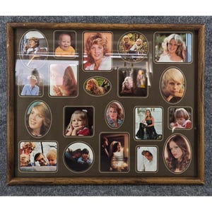 May include: A rectangular wooden picture frame containing a collage of seventeen individual photographs of various people. The photos are arranged in a mix of oval and square shapes against a dark brown background, showcasing portraits and candid shots.