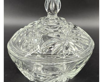 May include: A clear, faceted glass candy dish with a lid. The dish has a rounded shape with a starburst pattern on the lid and sides. The lid has a decorative finial. The glass is transparent, allowing light to pass through.