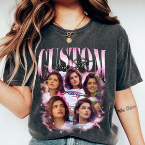 May include: Dark gray t-shirt with a pink and white graphic that says "CUSTOM Your Text". The graphic features multiple images of a woman with brown hair. The shirt is a vintage style.