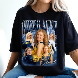 Könnte beinhalten: Schwarzes T-Shirt mit einem Grafikdesign mit dem Text "CHEER AUNT" in einer blauen, metallischen Schriftart. Das Design enthält mehrere Bilder einer lächelnden Person in Cheerleader-Kleidung mit dem Namen "Olivia" in Schreibschrift.