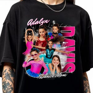May include: Black t-shirt with a collage of young dancers, the name "Adalyn" in cursive, and the words "DAVIS" in pink. "Dance Mom" is written at the bottom of the design.