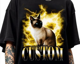 May include: Black t-shirt featuring a Siamese cat with blue eyes, set against a backdrop of yellow lightning. The word "CUSTOM" is displayed in a gold, stylized font across the bottom of the image. The shirt is made of a soft material.
