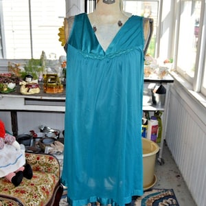 Op de afbeelding: Een mouwloos, blauwgroen nachthemd met een V-hals en een gerimpeld detail over de borst. Het kledingstuk is gemaakt van een gladde, lichtgewicht stof en heeft een losvallend, vloeiend silhouet dat tot halverwege de dij reikt.