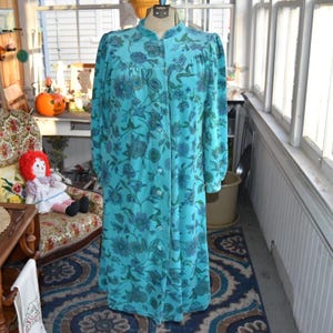May include: A vintage turquoise robe with a floral pattern in shades of blue and green. The long-sleeved robe has a button-up front and a mandarin collar. The robe is displayed on a mannequin.