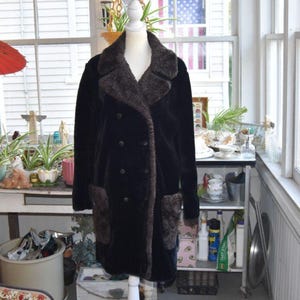 May include: A double-breasted coat in black with a dark brown faux fur collar and matching faux fur pocket accents. The coat features a wide lapel, long sleeves, and a button-front closure, displayed on a white mannequin torso.