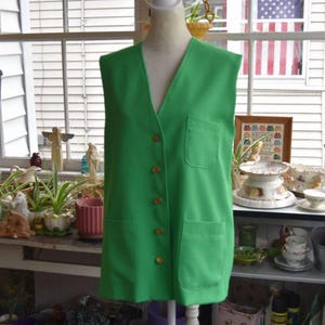May include: A sleeveless vest in a vibrant grass green color featuring a V-neckline, a front button closure with five matching buttons, one chest pocket on the left side, and two larger patch pockets positioned at the lower front of the garment.