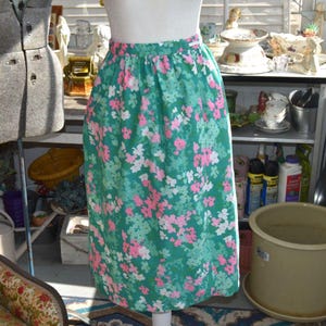 May include: A knee-length skirt with a green background and a floral pattern in pink, white, and light green. The skirt has an elastic waistband and a straight cut. The skirt is displayed on a mannequin.
