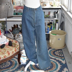 May include: Light blue denim jeans with a wide leg design. The jeans are displayed on a white mannequin leg. The jeans have a button and zipper closure and pockets. The jeans are a vintage style.