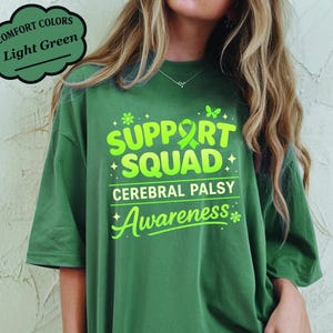 Op de afbeelding: Lichtgroen t-shirt met de woorden "SUPPORT SQUAD CEREBRAL PALSY Awareness" in felgroen. Het shirt heeft een relaxte pasvorm en is gemaakt van een zacht materiaal. Het shirt heeft ook een lichtgroene lintafbeelding.