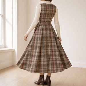 K&ouml;nnte beinhalten: Ein &auml;rmelloses Midikleid mit braunem, beigem und grauem Karomuster, ausgestattet mit einem figurbetonten Oberteil, einer durch einen passenden G&uuml;rtel definierten Taille und einem weiten, plissierten Rock &uuml;ber einem cremefarbenen Langarmshirt.