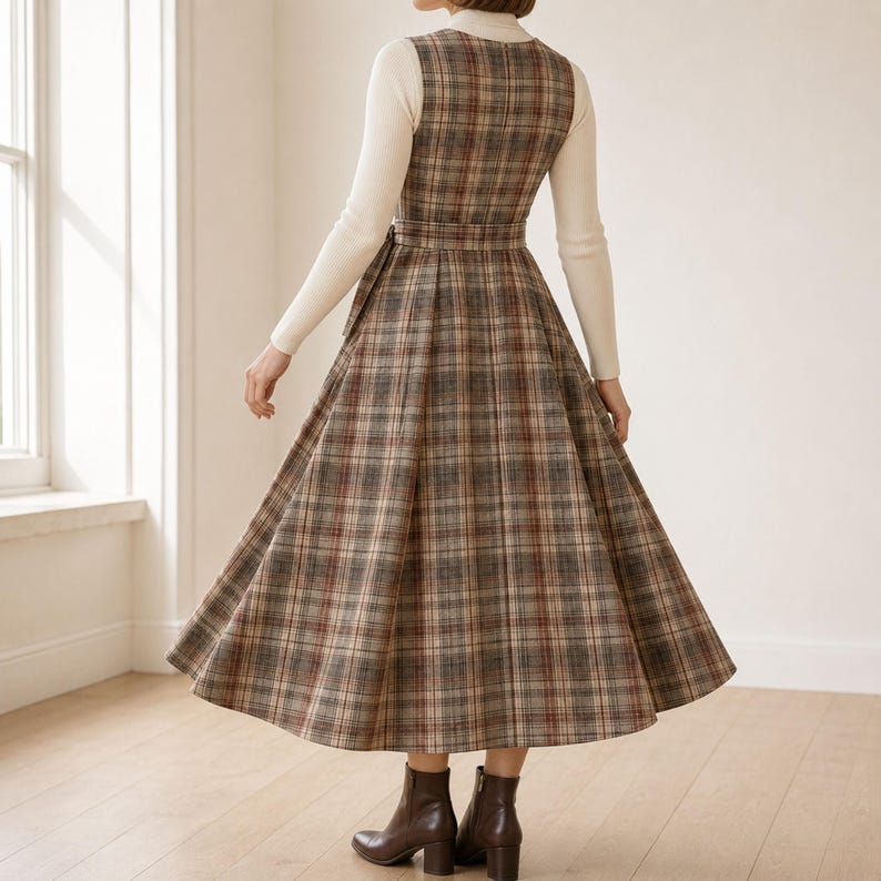 K&ouml;nnte beinhalten: Ein &auml;rmelloses Midikleid mit braunem, beigem und grauem Karomuster, ausgestattet mit einem figurbetonten Oberteil, einer durch einen passenden G&uuml;rtel definierten Taille und einem weiten, plissierten Rock &uuml;ber einem cremefarbenen Langarmshirt.