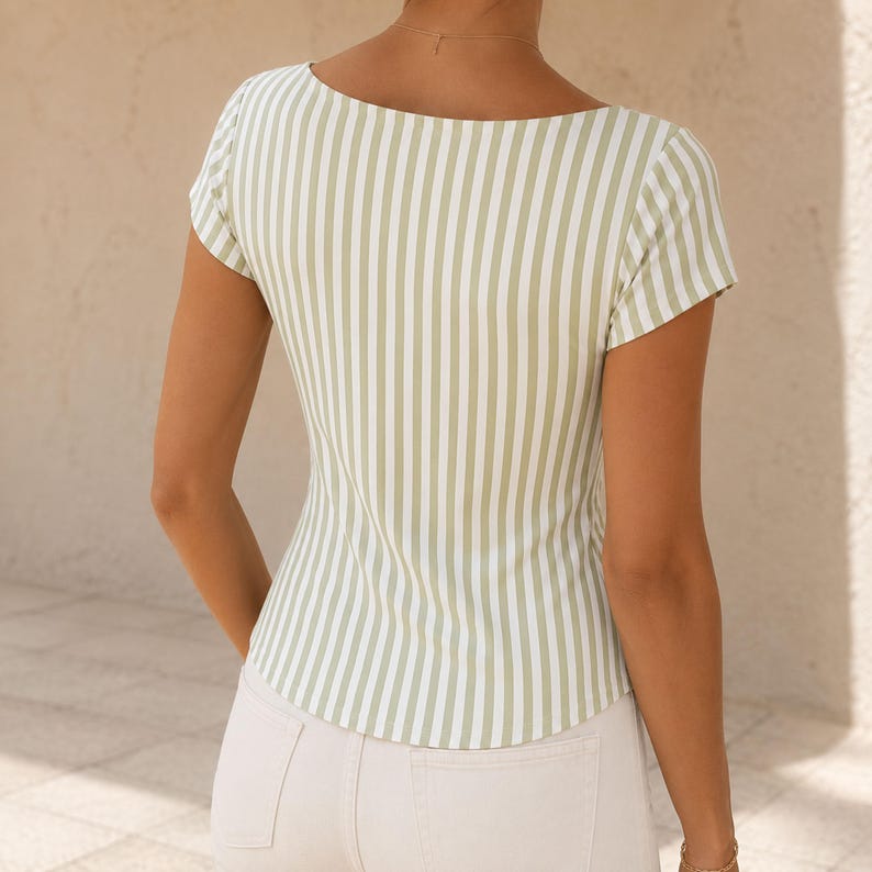 May include: A short-sleeved top featuring a vertical striped pattern in sage green and white. The garment has a square neckline and a fitted silhouette, paired with light-colored pants. The design includes a straight hemline at the waist.
