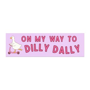 Könnte beinhalten: Rechteckiger Aufkleber mit hellviolettem Hintergrund. Eine weiße Cartoon-Ente fährt mit einem rosa Roller nach links. Der Text "ON MY WAY TO DILLY DALLY" ist rosa, umrandet von einem dunkleren Rosa.