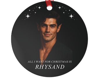 Op de afbeelding: Ronde kerstversiering met een portret van een man met puntoren, tegen een donkere achtergrond met sterren. De tekst "ALL I WANT FOR CHRISTMAS IS RHYSAND" staat onderaan. Een rood lint is bevestigd om op te hangen.