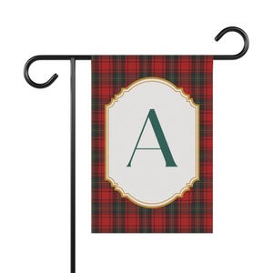 Könnte beinhalten: Eine Gartenflagge mit einem rot, schwarz und grün karierten Muster. Die Flagge hat eine weiße Mitte mit einem goldenen Rand und einem großen grünen Buchstaben "A". Sie wird auf einem schwarzen Metallständer präsentiert.