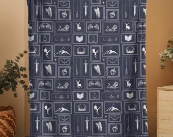 May include: A navy blue blanket with a repeating pattern of white fantasy-themed illustrations. The design includes swords, wings, mountains, books, and other magical elements. The blanket is held up by a person.