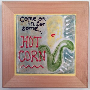 Può includere: Una piastrella incorniciata con un designo dipinto a mano. La piastrella presenta un designo astratto verde e giallo con le parole "Come on in for some... HOT CORN" scritte in vernice rossa e nera.