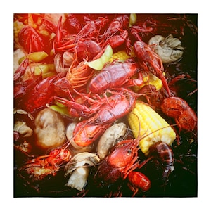May include: A close-up of a seafood boil with red crawfish, yellow corn on the cob, mushrooms, and a lime wedge. The crawfish are the main focus, their colour contrasting with the other ingredients. A delicious meal.