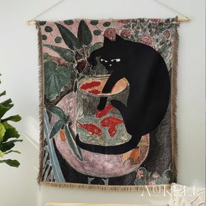 May include: A woven wall hanging featuring a black cat reaching into a bowl with red fish. The artwork has a vintage aesthetic with a floral and botanical background. The wall hanging is framed by a wooden rod.