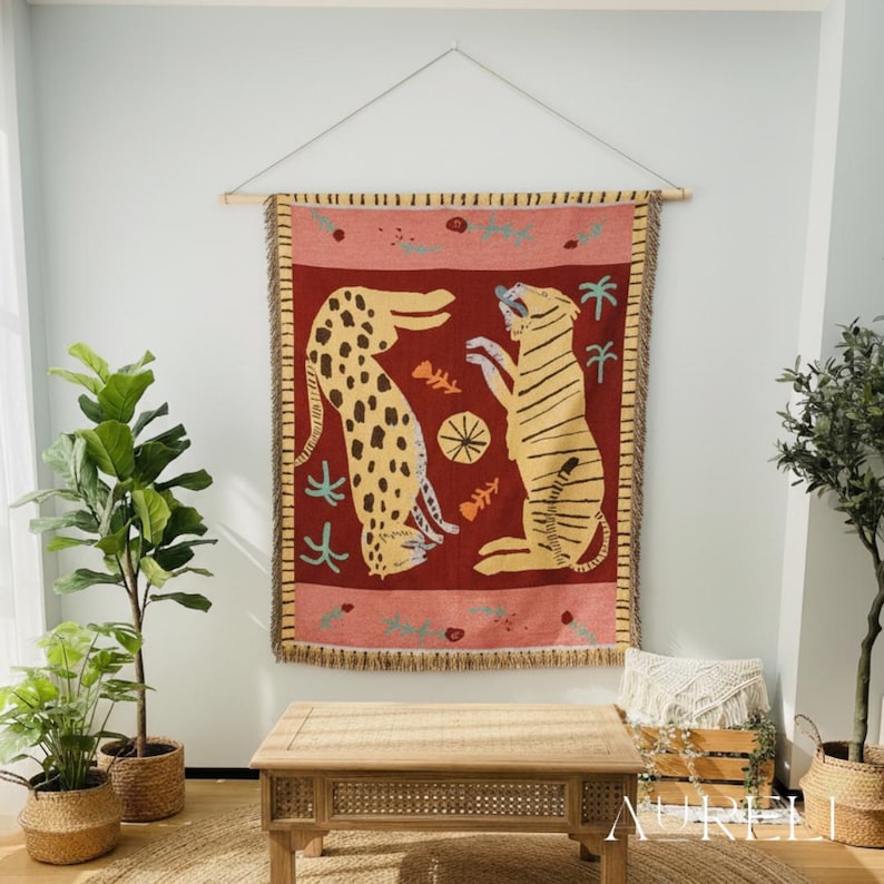 May include: A tapestry featuring two stylized big cats, a leopard and a tiger, against a red background. The tapestry is rectangular with a fringed border and is suspended from a wooden rod. The design includes fish bones and palm trees.