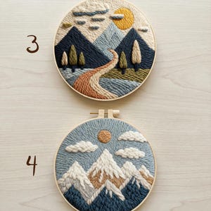 May include: Two embroidered landscape art pieces in wooden hoops. One features a mountain scene with a river, trees, and a sun. The other depicts snow-capped mountains, clouds, and a sun. The word "AURELI" is at the bottom.