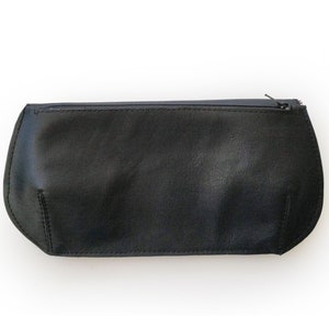May include: A black leather pencil case with a zipper closure. The case has a rounded shape and is made of a smooth, matte material. The zipper is dark and runs along the top of the case.