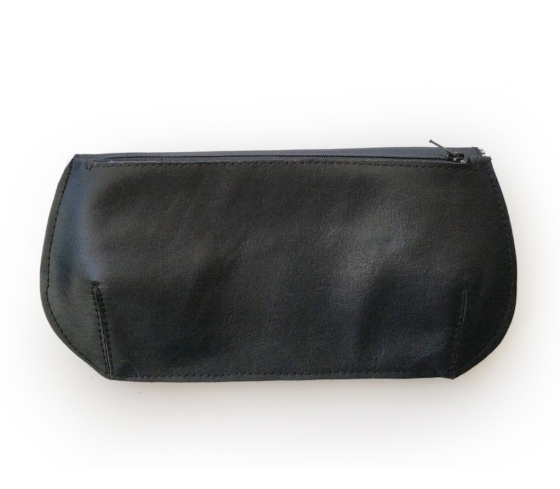 May include: A black leather pencil case with a zipper closure. The case has a rounded shape and is made of a smooth, matte material. The zipper is dark and runs along the top of the case.