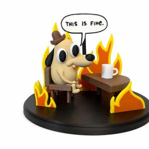 May include: A figurine depicting a cartoon dog wearing a hat, sitting in a chair, surrounded by flames. A speech bubble above the dog reads "THIS IS FINE." A small table holds a white mug. The base is black.