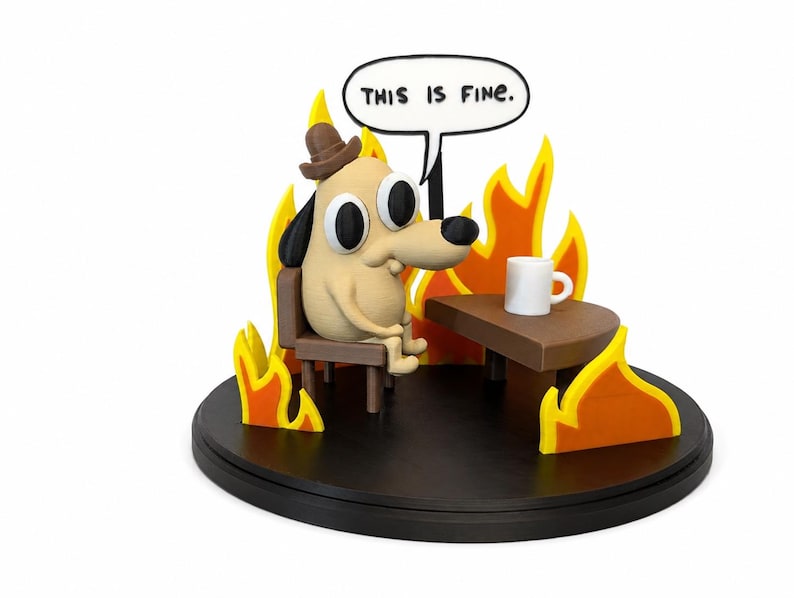 May include: A figurine depicting a cartoon dog wearing a hat, sitting in a chair, surrounded by flames. A speech bubble above the dog reads "THIS IS FINE." A small table holds a white mug. The base is black.
