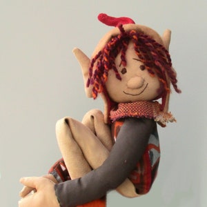 May include: A handmade plush elf doll with red and brown yarn hair, a brown felt face, and a red, orange and brown patterned outfit.