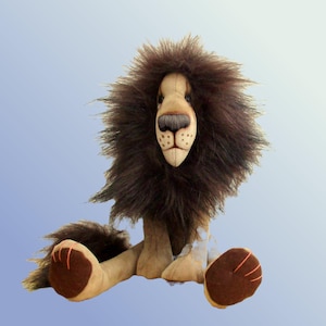 May include: A plush lion toy featuring a tan fabric body and a large, dark brown faux fur mane. The lion has a stitched nose, dark brown paw pads with orange thread accents, and a long, bushy tail. The face is constructed from light tan fabric.