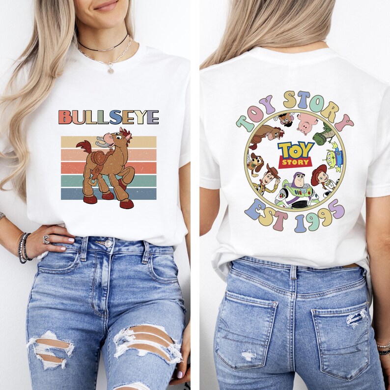 Może przedstawiać: Biała koszulka z grafiką Bullseye z Toy Story i retro wzorem zachodu słońca. Tył koszulki przedstawia grafikę Toy Story z napisem "Toy Story Est 1995" w okrągłym wzorze.