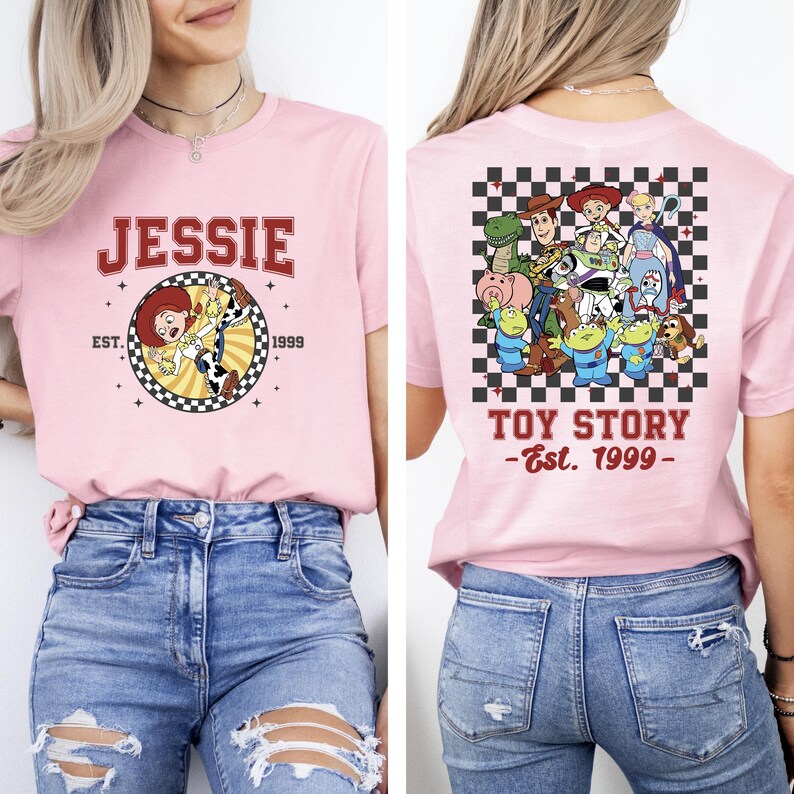 Puede incluir: Camiseta rosa claro con Jessie de Toy Story en la parte delantera, texto "JESSIE" encima de un gr&aacute;fico circular. La parte trasera tiene un patr&oacute;n de cuadros con personajes de Toy Story y el texto "TOY STORY - Est. 1999 -."