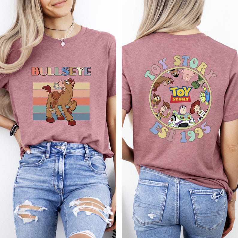 Może przedstawiać: Malinowa koszulka z grafiką Bullseye i napisem "BULLSEYE". Tył koszulki zdobi wz&oacute;r "Toy Story" z postaciami i napisem "EST 1995". Zabawny, kolorowy design dla fan&oacute;w filmu.