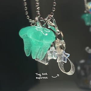 May include: A pair of translucent teal jellyfish charms hanging from a silver ball chain. Clear star-shaped charms and a silver clasp are also attached. The text "Tag Sold separate" is visible.