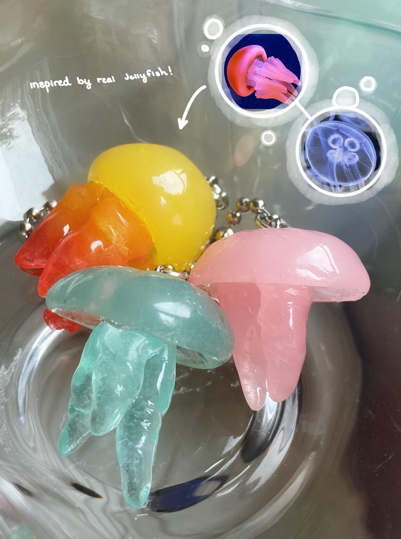 May include: Colorful jellyfish-shaped keychains in yellow, orange, pink, and teal. The keychains are inspired by real jellyfish, as indicated by the text in the image. The keychains are attached to silver chains.