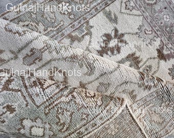 May include: Close-up of a rolled-up, intricately patterned rug. The rug features a muted color palette of beige, gray, and brown, with floral and geometric designs. The text "GulnajHandKnots" is visible on the rug.