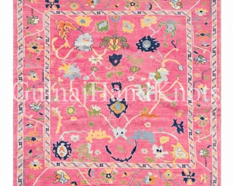 May include: A square area rug with a vibrant pink background featuring a multi-colored floral pattern in shades of blue, yellow, green, and orange. The rug has a decorative border and white fringe on the edges. The text GulnajHandKnots is visible.