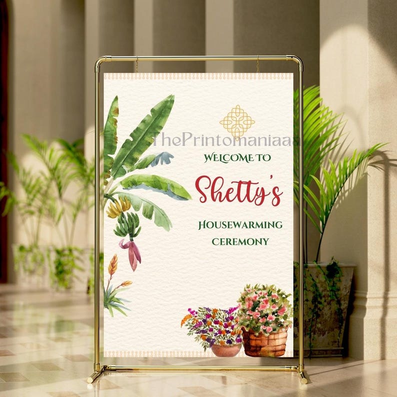 May include: A gold metal framed sign with the text "Welcome to Shetty's Housewarming Ceremony." The sign features watercolor illustrations of banana leaves, flowers, and a gold geometric design. The background is a cream color.