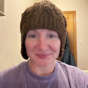 May include: A brown, knitted hat with ear flaps. The hat is made of a textured yarn and has a close-fitting design. The hat is a warm accessory for cold weather.