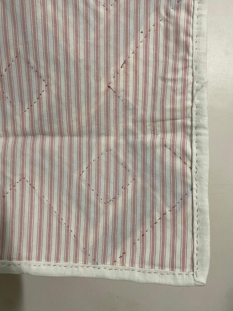 May include: Close-up of a quilted fabric with a white border. The fabric features vertical red and white stripes with a diamond pattern stitched across the surface. The border is a solid white fabric.