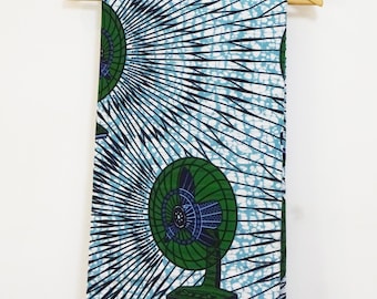 May include: A length of fabric featuring a repeating pattern of green electric fans on a light blue background. The design includes dark blue radiating lines and white crackle-like textures that create a dynamic visual effect across the textile.