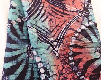 May include: A folded textile with a batik design. The fabric features a mix of colors, including teal, coral, and black. The pattern includes stylized leaf shapes, geometric designs, and white dot accents. The overall effect is a vibrant and artistic textile.
