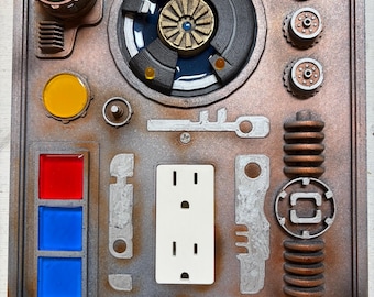 May include: A detailed, steampunk-style wall panel with various mechanical components. Features a central circular design, multiple dials, buttons, and a standard electrical outlet. The color scheme includes shades of gray, brown, and copper, with accents of green, yellow, red, and blue.