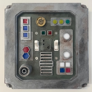 May include: A weathered, gray control panel with various colored buttons, switches, and indicator lights. The panel features a circular dial, rectangular and hexagonal buttons in red, blue, and green, and two white toggle switches. The design has a retro-futuristic aesthetic.