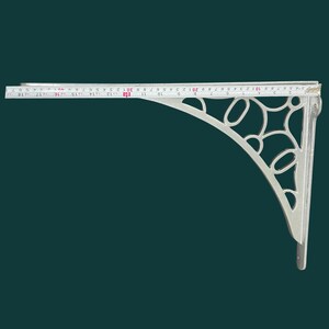 K&ouml;nnte beinhalten: Ein silberfarbener Regaltr&auml;ger mit einem verzierten, durchbrochenen Design. Der Tr&auml;ger ist etwa 46 cm lang und hat eine gebogene St&uuml;tze mit ovalen und kreisf&ouml;rmigen Aussparungen. Ein Ma&szlig;band liegt am oberen Rand.