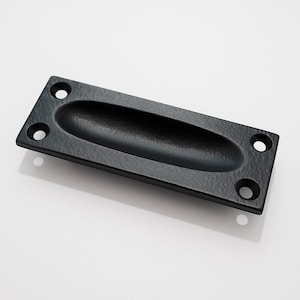 May include: A black rectangular recessed pull with an oval finger grip. The hardware has a textured surface and four screw holes. This cabinet pull is a classic design for drawers and doors.
