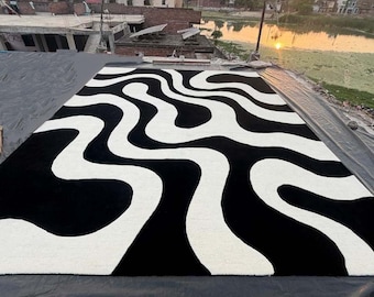 May include: A rectangular area rug featuring a high-contrast black and white pattern of fluid, organic, wavy lines that stretch across the entire surface. The design consists of thick, interconnected curves creating a bold, abstract visual effect.