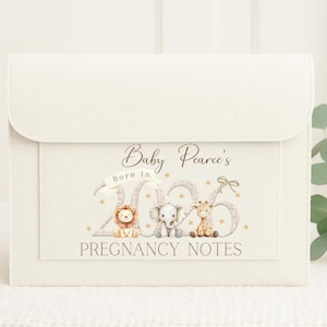 May include: A cream-coloured pregnancy notes folder with a flap closure. The front features the text "Baby Pearce's Born In 2026" with illustrations of a lion, elephant, and giraffe. The words "PREGNANCY NOTES" are below the illustrations.