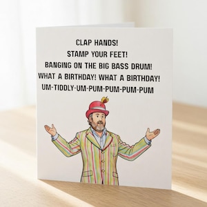 May include: A birthday card with the text "CLAP HANDS! STAMP YOUR FEET! BANGING ON THE BIG BASS DRUM! WHAT A BIRTHDAY! WHAT A BIRTHDAY! UM-TIDDLY-UM-PUM-PUM-PUM-PUM." The card shows a man in a striped suit and a red hat.